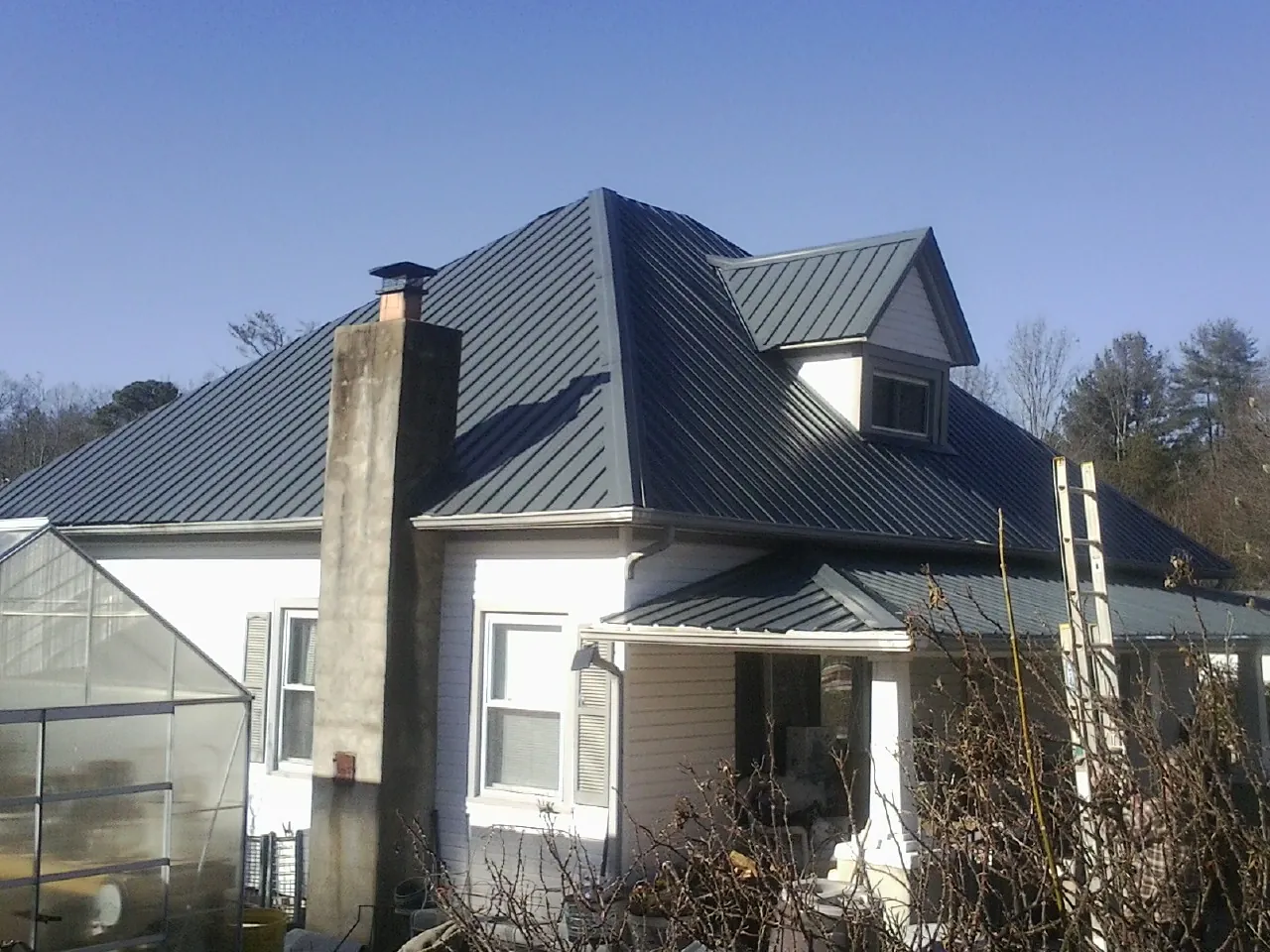 Dark blue standing seam metal roof on a white farmhouse with dormer — Slate & Tile Roof Repair by Roofing Brothers in Faison