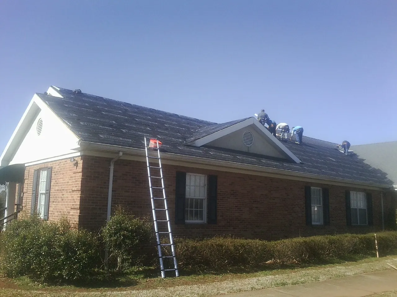 Crew tearing shingles off a brick ranch roof with a ladder set — Metal Roof Repair work by our crew in Faison