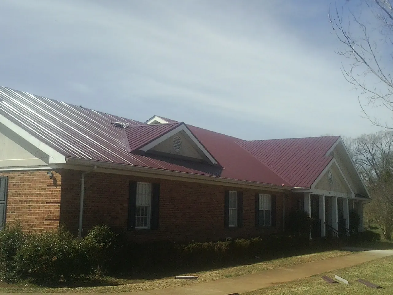 Red metal roof with gabled entries on a long brick building, from a Hail Damage Roof Repair job in Faison