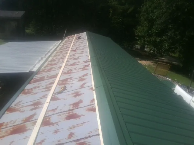 Old rusted panels beside newly installed green metal roofing — Wind Damage Roof Repair by Roofing Brothers in Faison