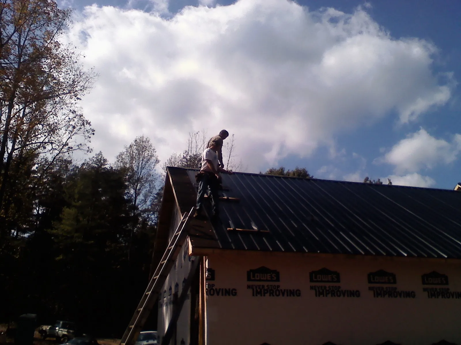 Roofer fastening dark metal panels high against a cloudy sky, from a Roof Inspection job in Faison