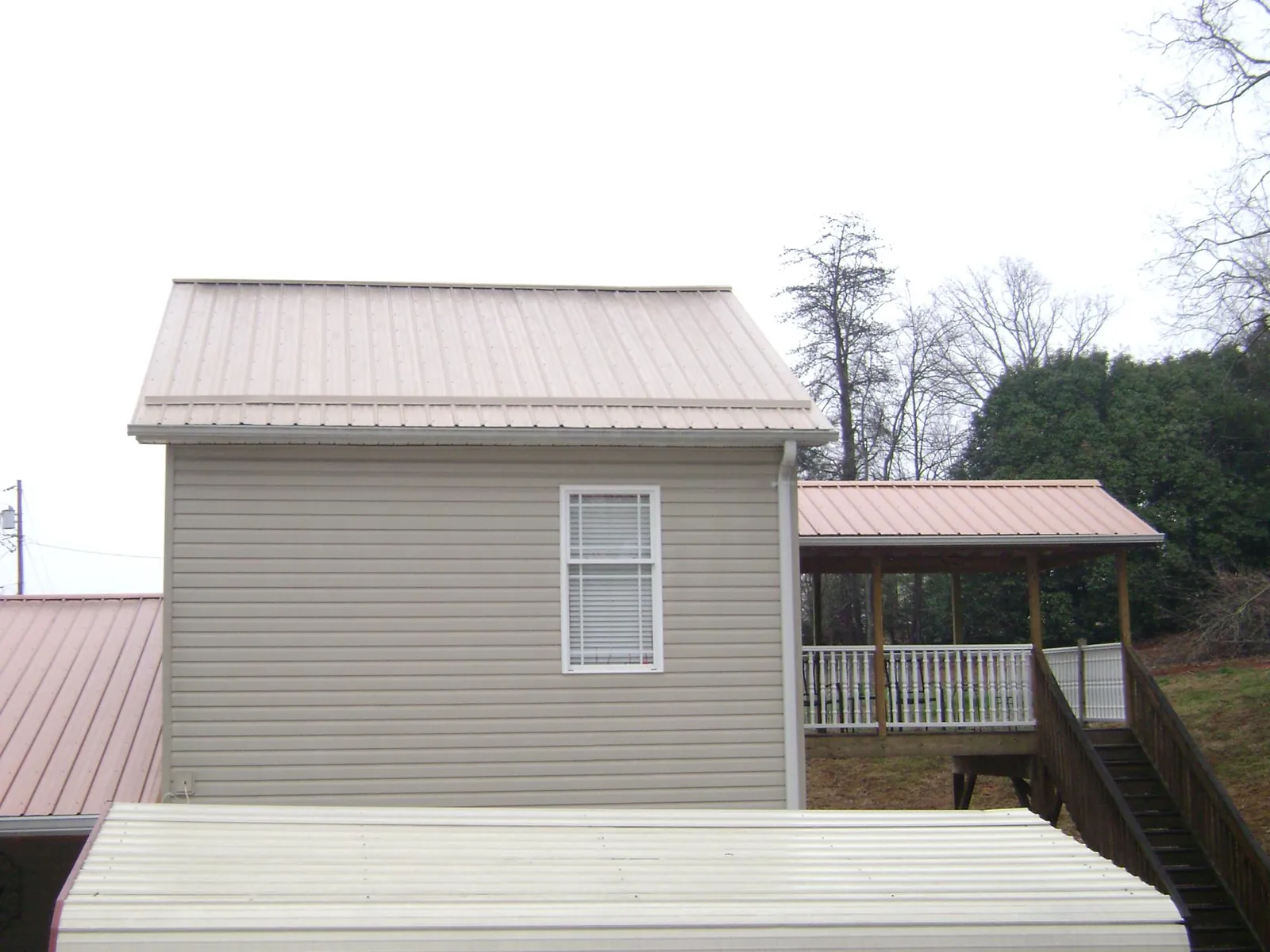 Tan metal roofs on a two story addition and attached porch, from a Roof Replacement job in Faison